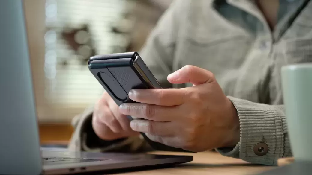 Person using mobile phone and laptop with cup of coffee on desk