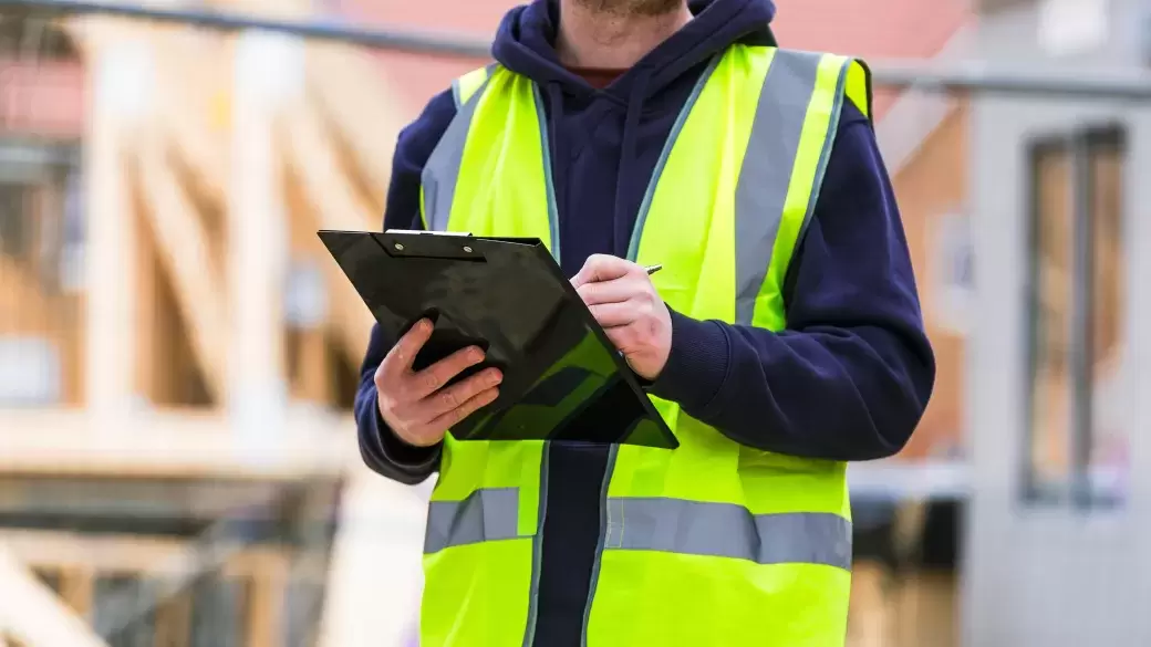 Builder on site wearing high visibility jacket and completing a checklist on a clipboard