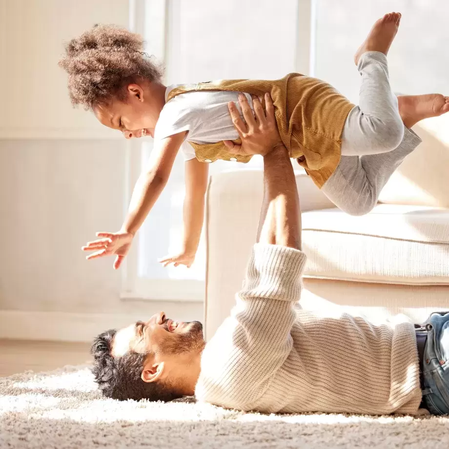 A dad lying down and his young daughter above him
